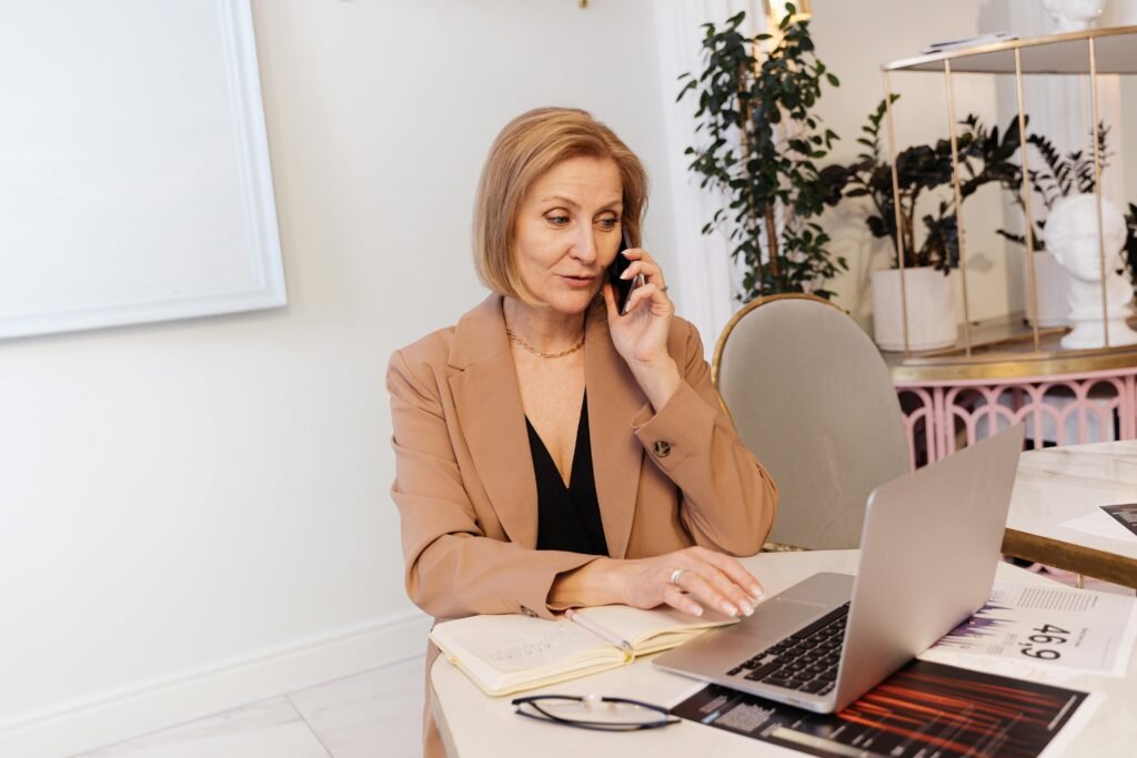 Businesswoman multitasking, using laptop and phone in a modern office space.