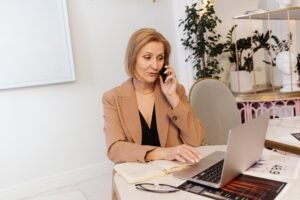 Businesswoman multitasking, using laptop and phone in a modern office space.