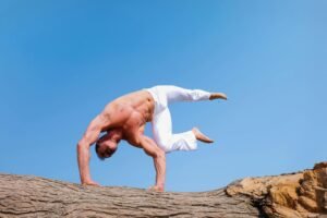 A man performs a dramatic handstand on rocks with a clear blue sky backdrop, showcasing fitness and balance.